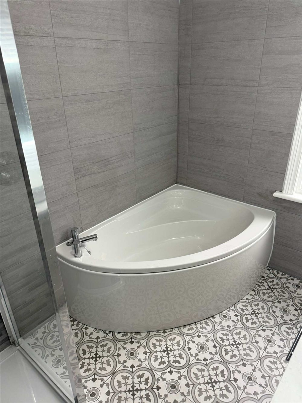 Corner bath with grey wall tiling