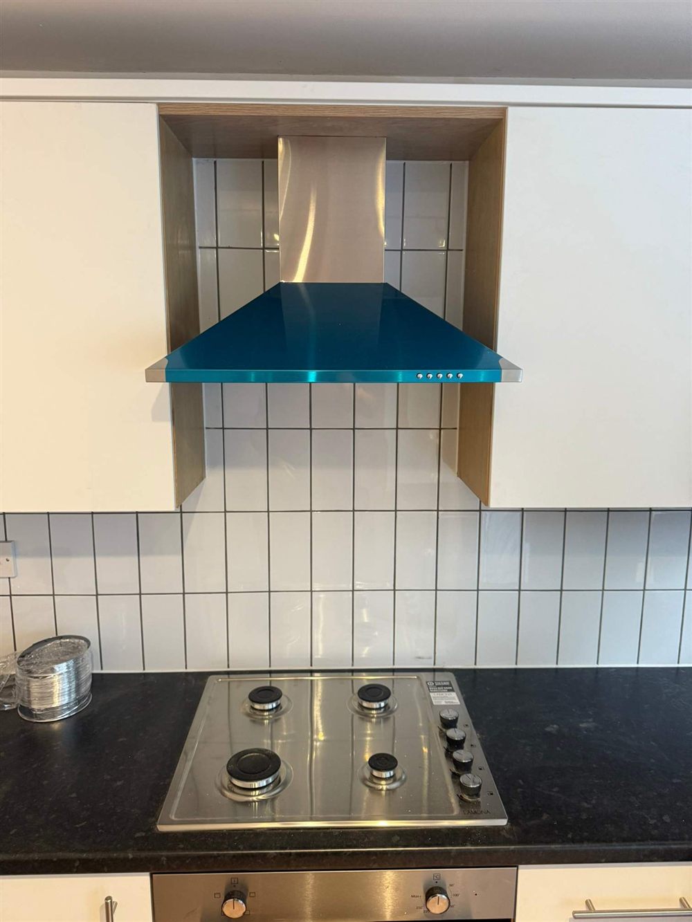 Gas hob with tiled splashback and blue extractor hood