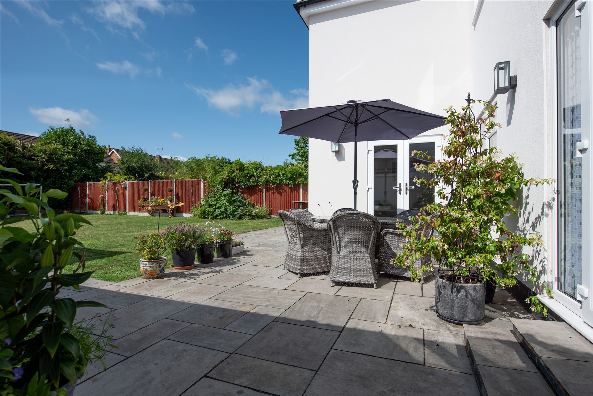 Back garden with grey paving patio and rattan furniture